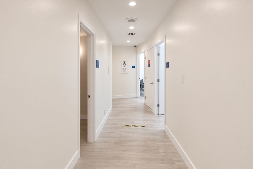 A clinic hallway with open doors, an eye chart, and light wood-look flooring. Illustrative photograph.